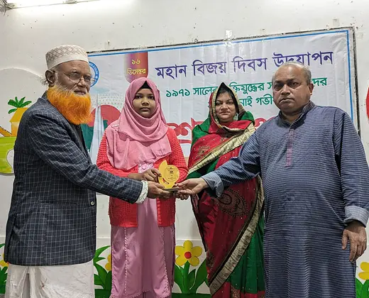 মহান বিজয় দিবস উদযাপন অনুষ্ঠানে একজন শিক্ষার্থীর হাতে ট্রফি তুলে দিচ্ছেন অতিথিরা